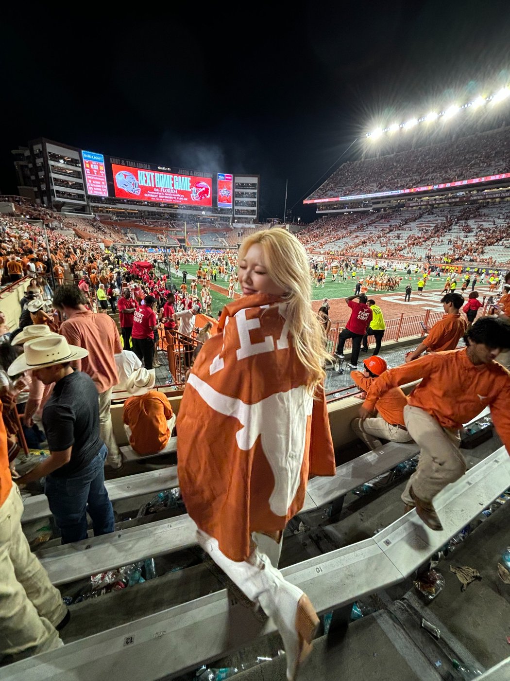 Photo of Jean Seo at Texas football game, wrapped in a burnt-orange flag.